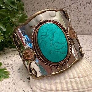 Wide metal cuff bracelet with turquoise color stone accent.